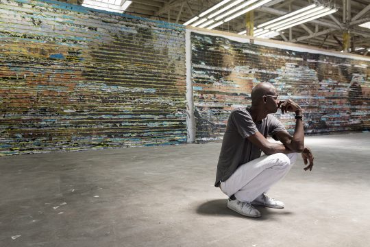 Mark Bradford, seen in his Los Angeles studio with a detail of Pickett's Charge, 2017. Mixed media. Courtesy of the artist and Hauser & Wirth. Photo: Agata Gravante