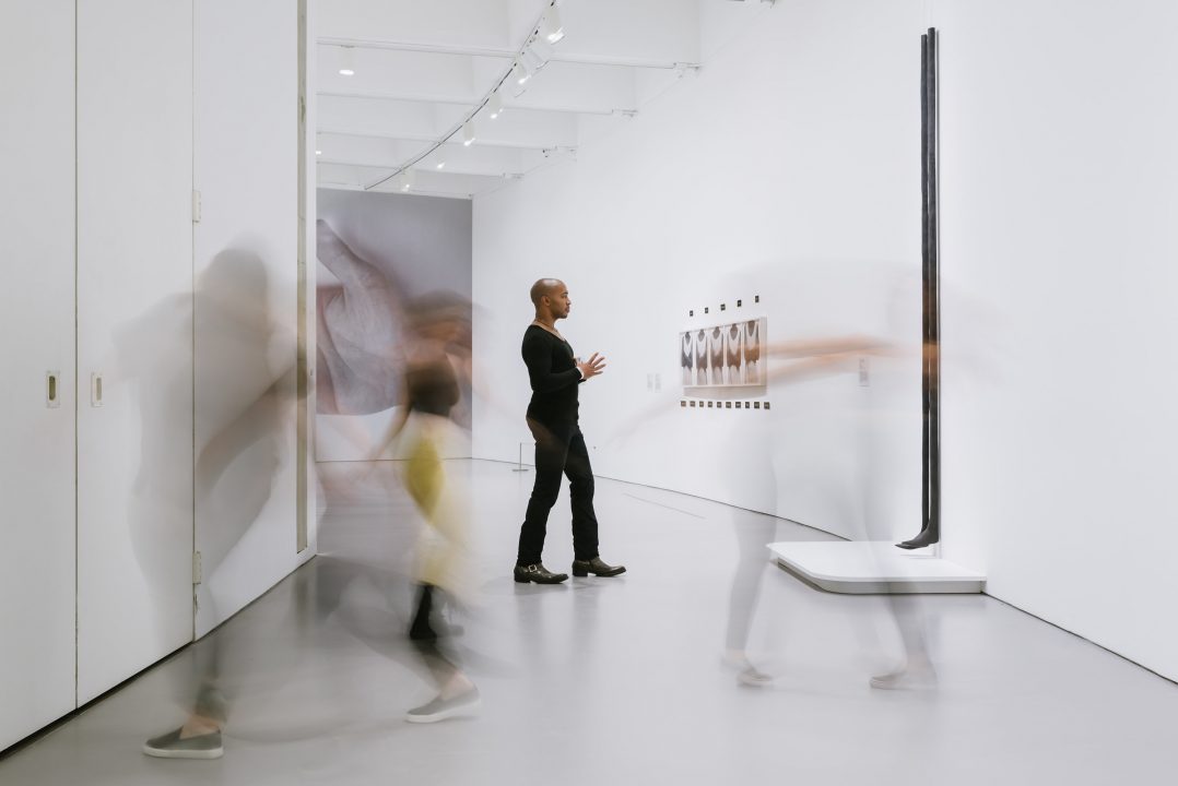 Visitor in gallery contemplates artwork as other visitors are moving