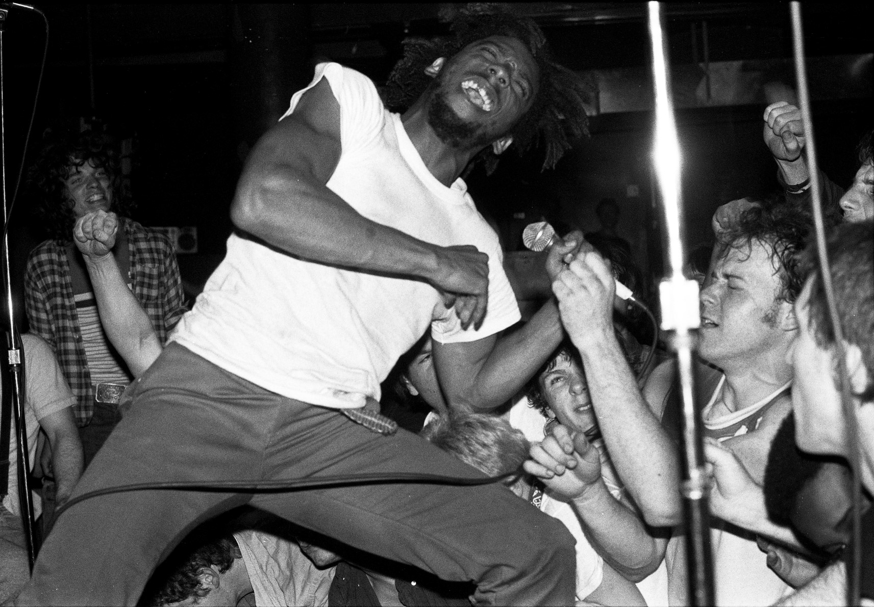 Black and white photo of punk musician performing surrounded by a crowd.