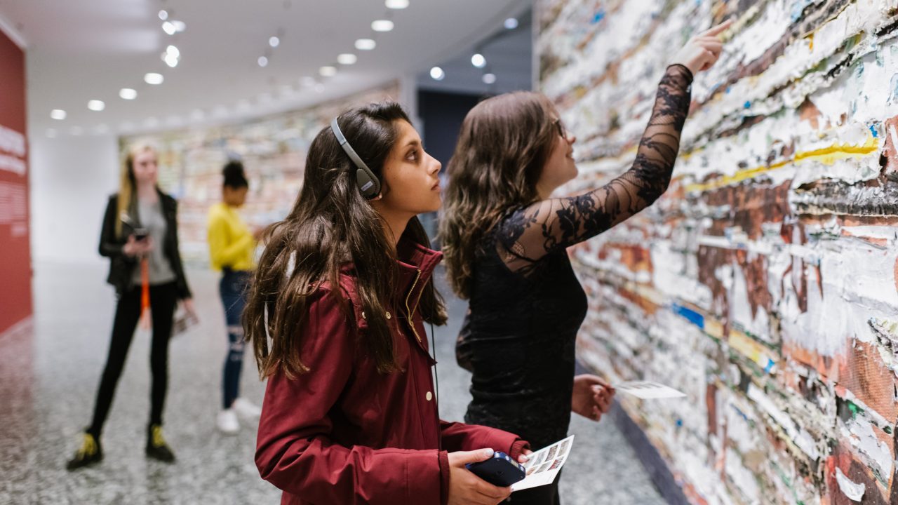 Visitor with headphones on looks at art work on wall.