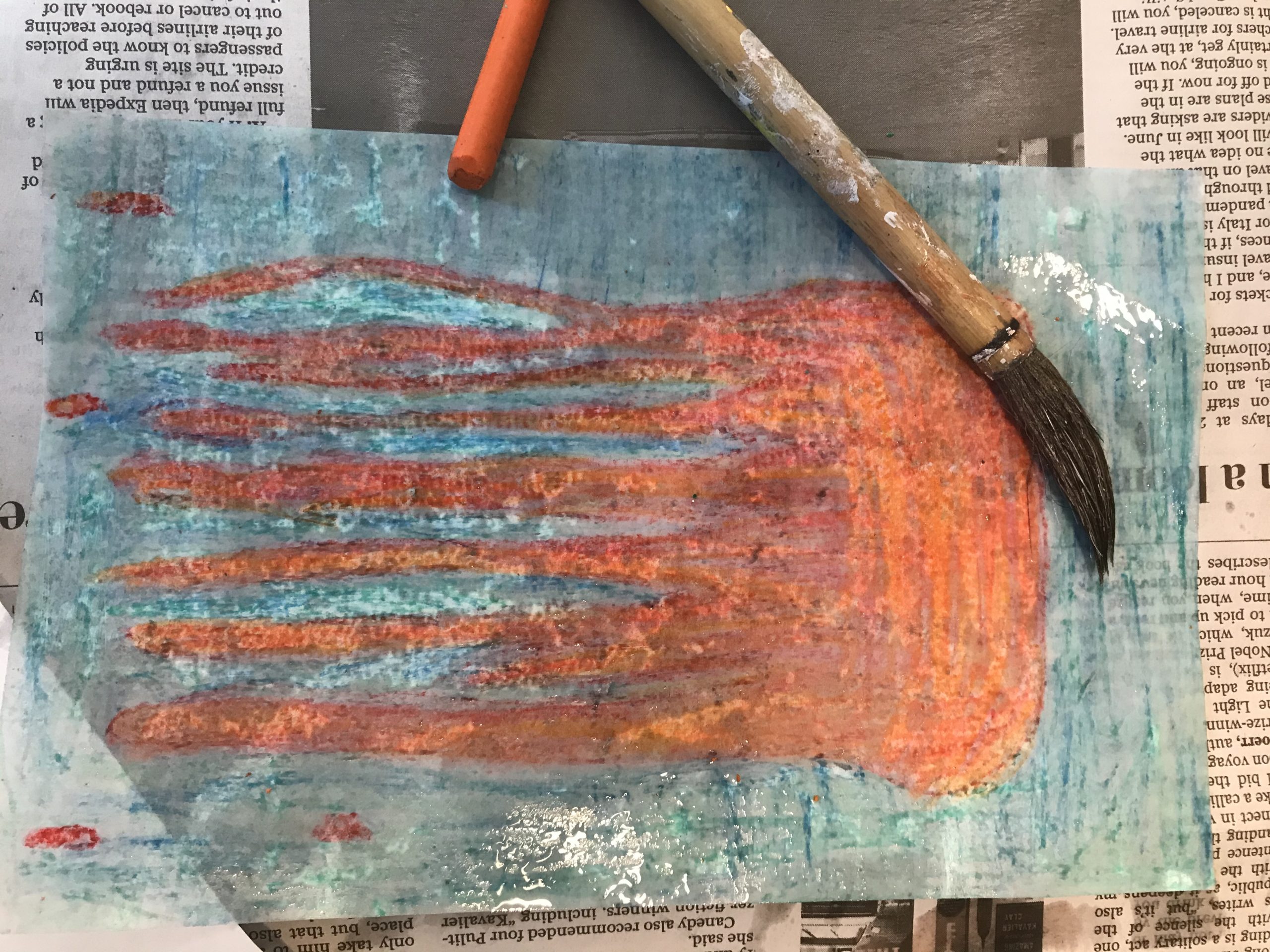 Paper with red and blue paint lays on top of a newspaper. A brush is laid across the paper.