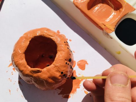 Orange clay pot being painted with black dots.