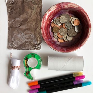 Dish with coins, toilet paper roll, markers, aluminum foil, tape, and fabric.