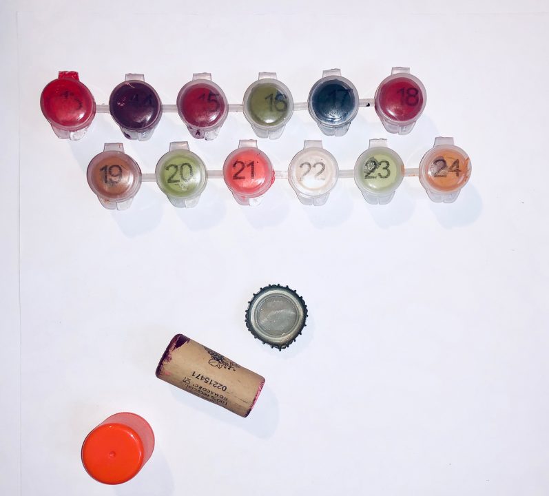 Various paints, cork, bottle cap, and film canister sitting on a white surface.