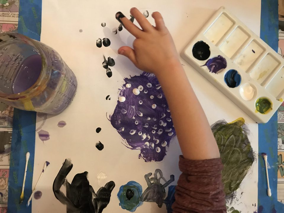 Hand reaches into frame to finger-paint black dots onto the piece of paper