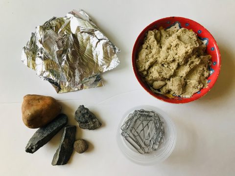 Foil, rocks, sand, and paperclips are displayed