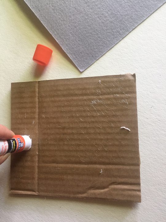 Hand applying glue to piece of square cardboard