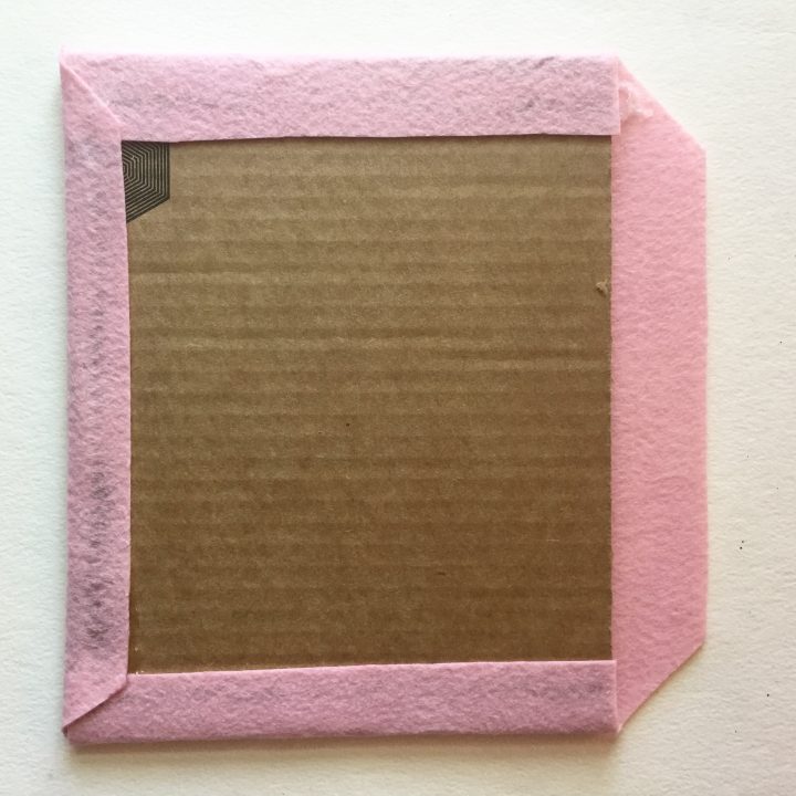 Pink felt with the corners cut off, wrapped around a rectangular piece of cardboard and glued at the back around the edges