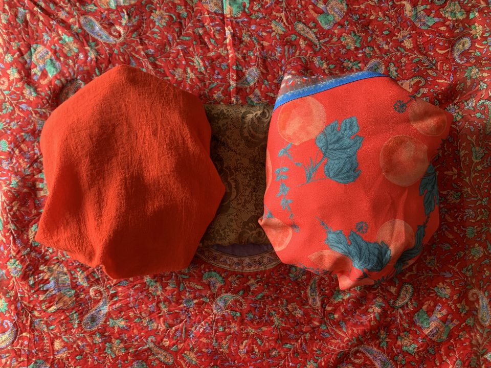 Two balled up shirts lie side by side on the red, paisley patterned scarf. One is plain red, the other is red with blue leaves.