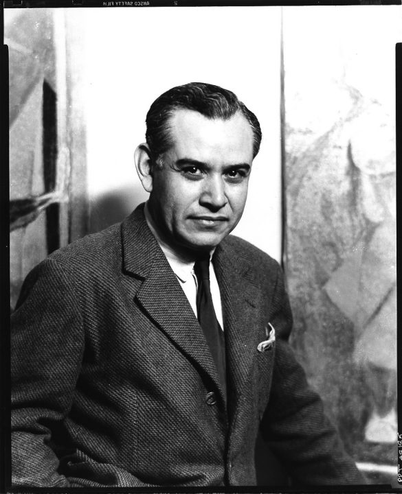 Black-and-white photograph of the artist sitting and smiling at the camera, his dark hair combed back, wearing a gray tweed jacket with white shirt and black tie.