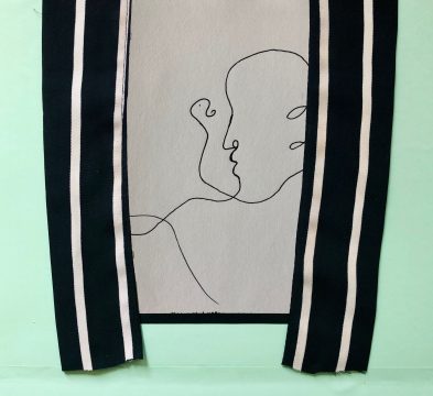 Against a mint green background, a white paper with black ink is flanked by two strips of black and white striped fabric.