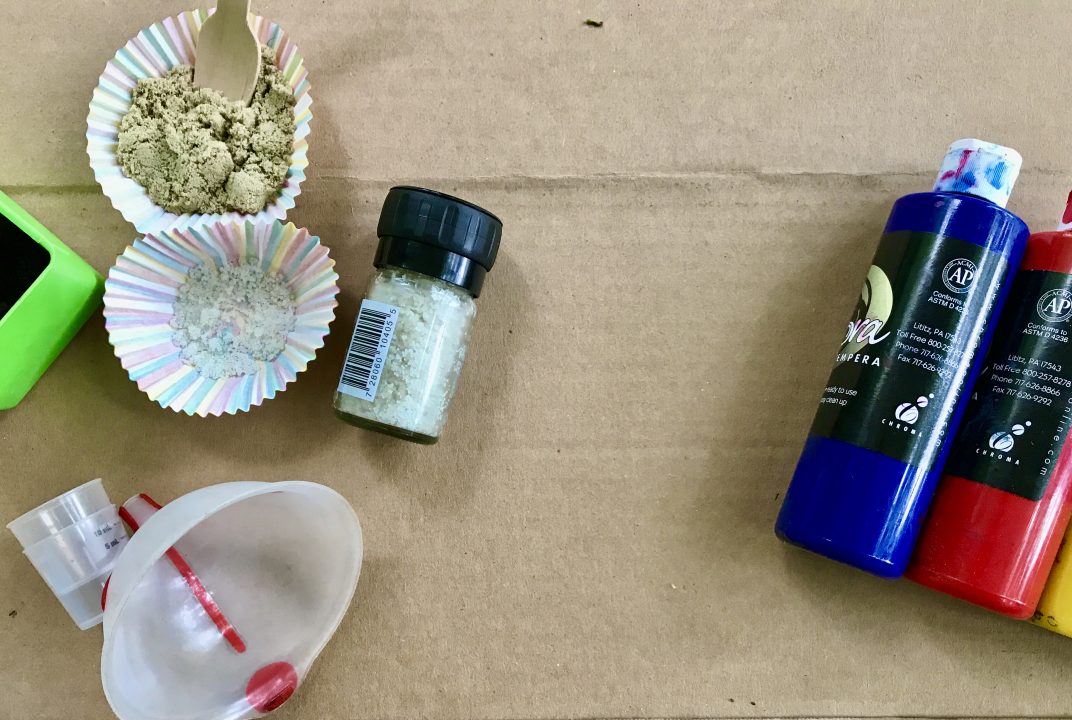 Cupcake liners containing sand and salt, salt grinder, medicine cups, plastic funnel, and bottles of paint