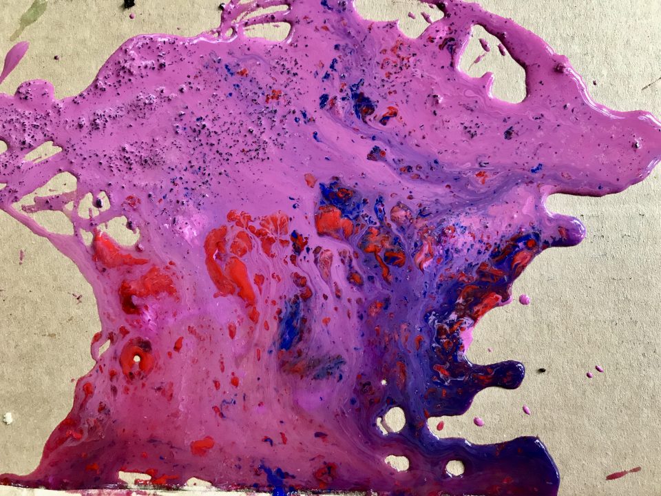 Cardboard surface with blue, red, pink, and purple paint mixing and puddling on it.