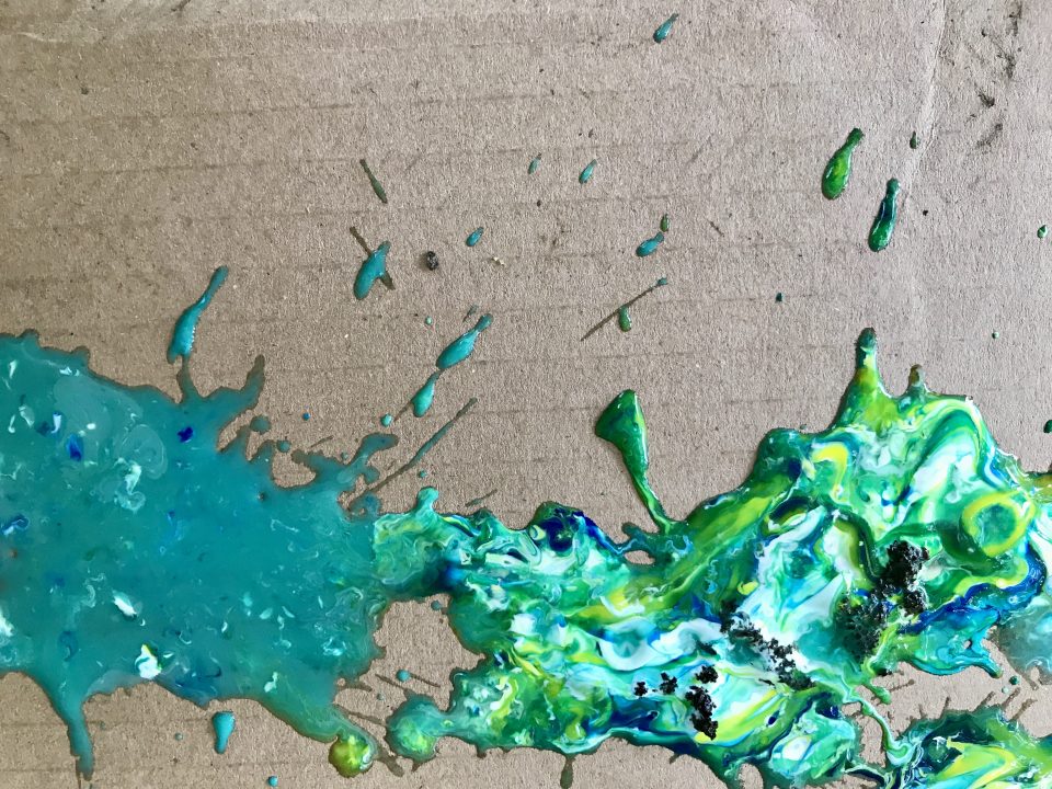 Cardboard surface with splatters of blue, green, and teal paint.