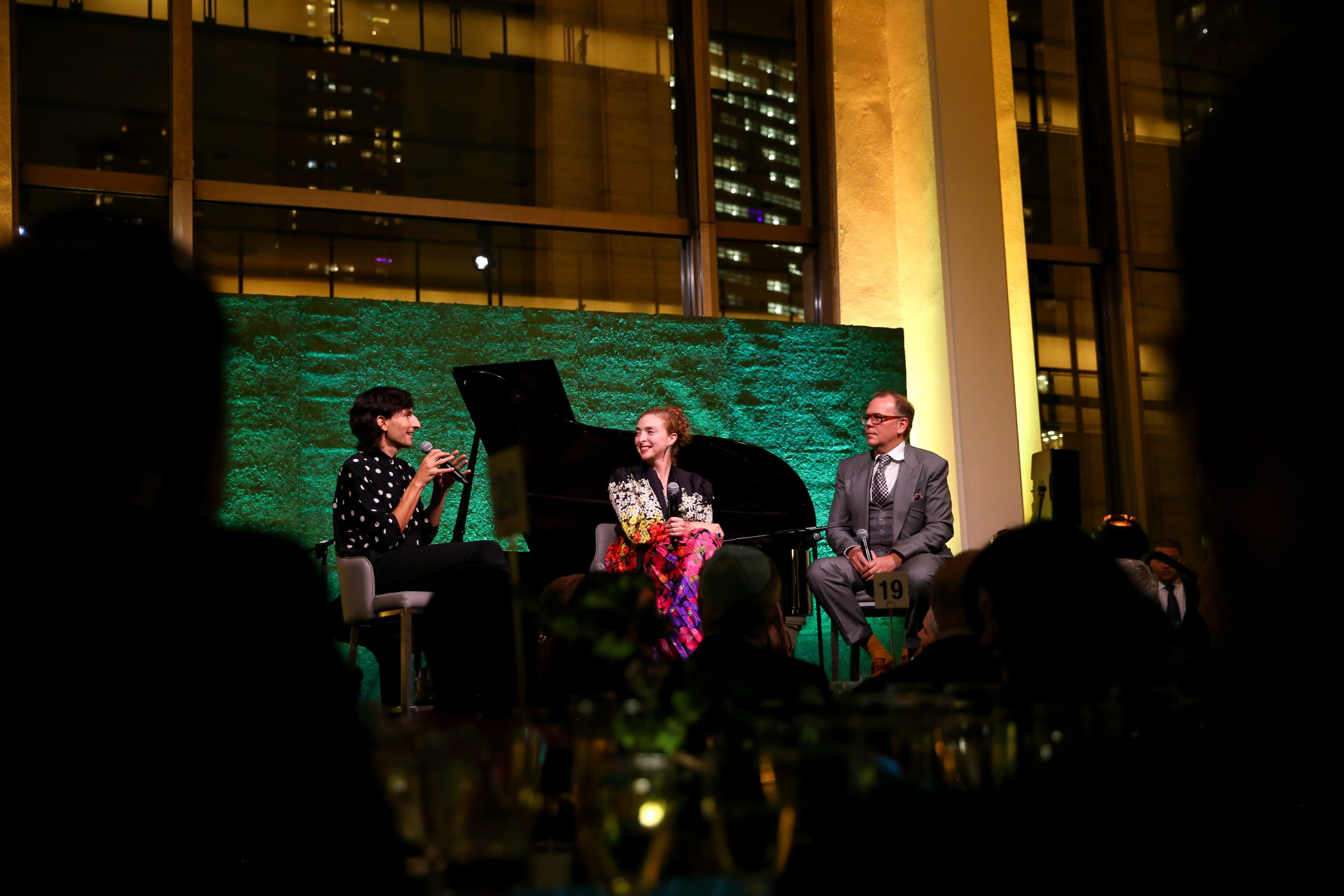 On stage are three speakers. Foreground is silhouette of the audience.