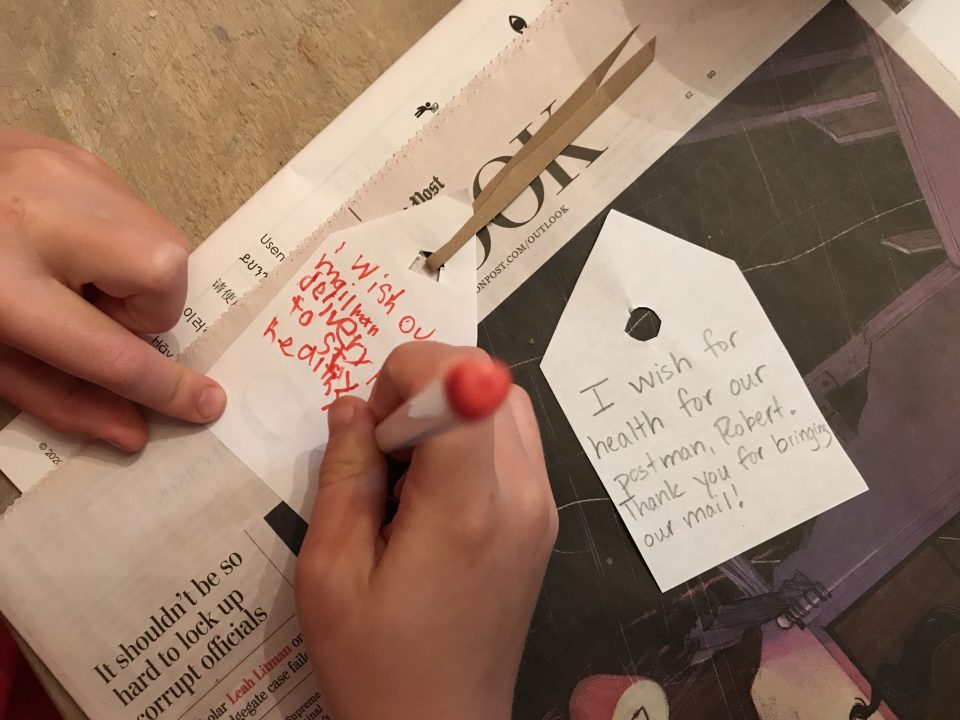 Two small pieces of white paper lying on a newspaper, one with writing in pencil, a hand uses a red marker to write on the other