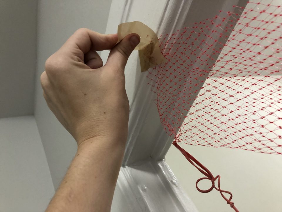 A hand affixes a red net to a door frame with a piece of masking tape.