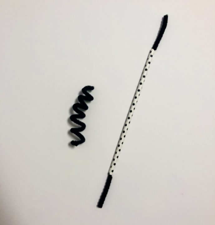 A spiral black pipe cleaner and white straw with black pipe cleaner inserted through it are displayed on a white background.