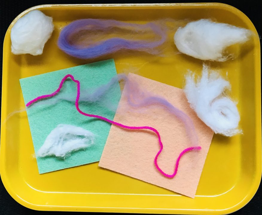 A rectangular yellow tray holds an arrangement of colorful felt, pink string and white cotton balls.