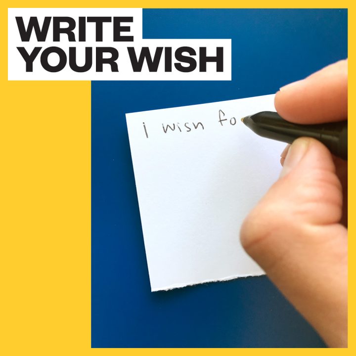 Text reads "write your wish" Hand holding pen is writing on white paper