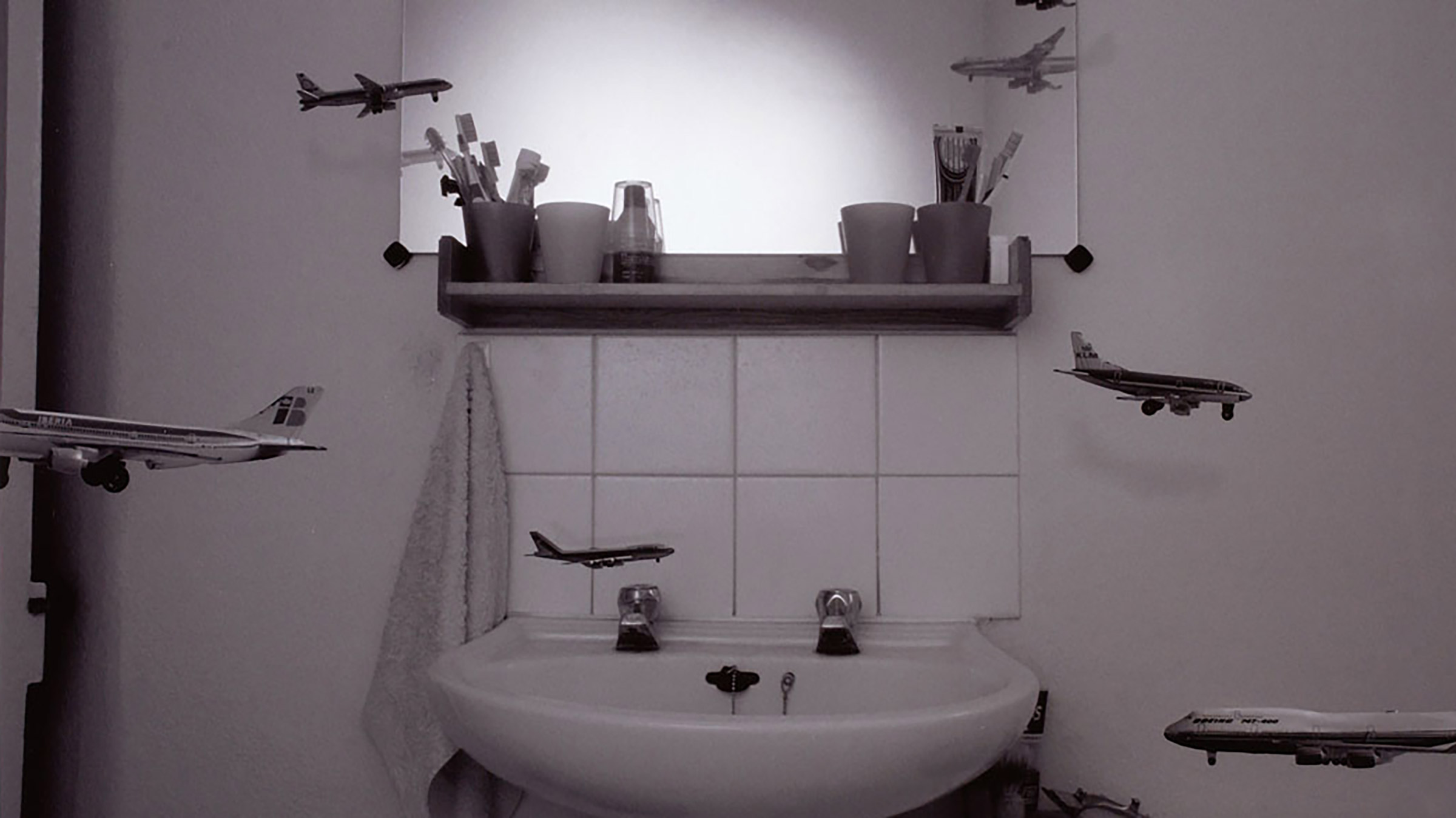 Black and white photo. Small miniature planes flying around in a bathroom.