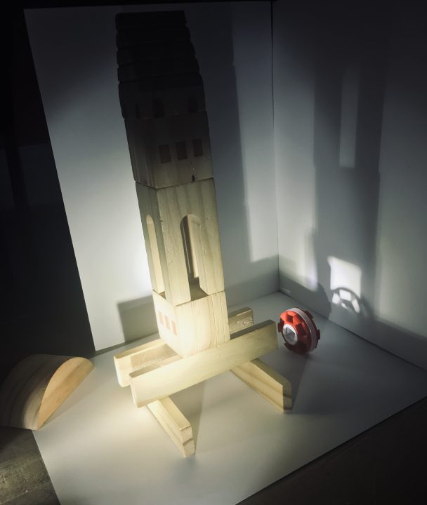 A tower of wood blocks casts two shadows on two adjacent white panels.