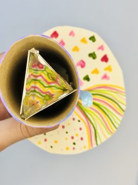 A triangular homemade kaleidoscope inside a round barreled-viewer examines a round work on paper featuring curved lines, dots and hearts.