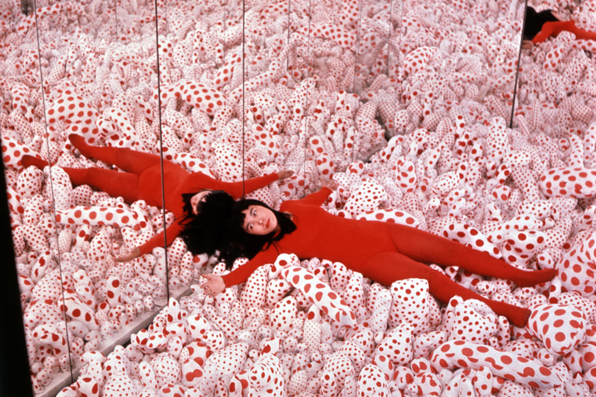 Artist Yayoi Kusama dressed in red lays in one of her infinity rooms