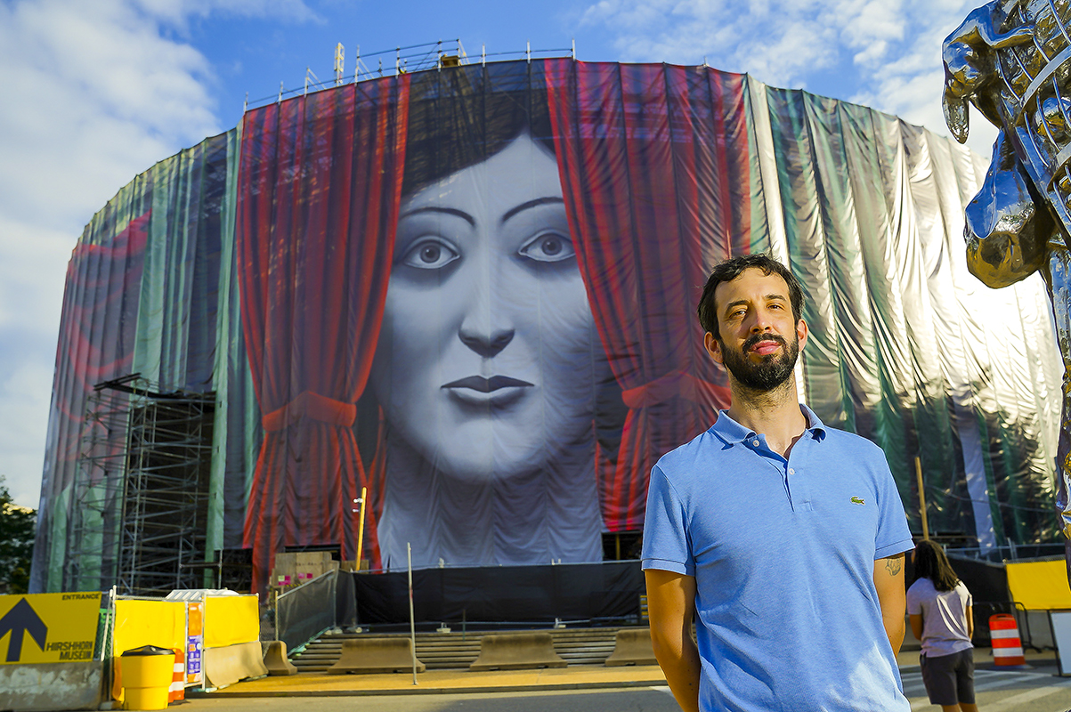 The artist Nicolas Party stands in front of the Hirshhorn Museum, which has been wrapped with his artwork Draw the Curtain.