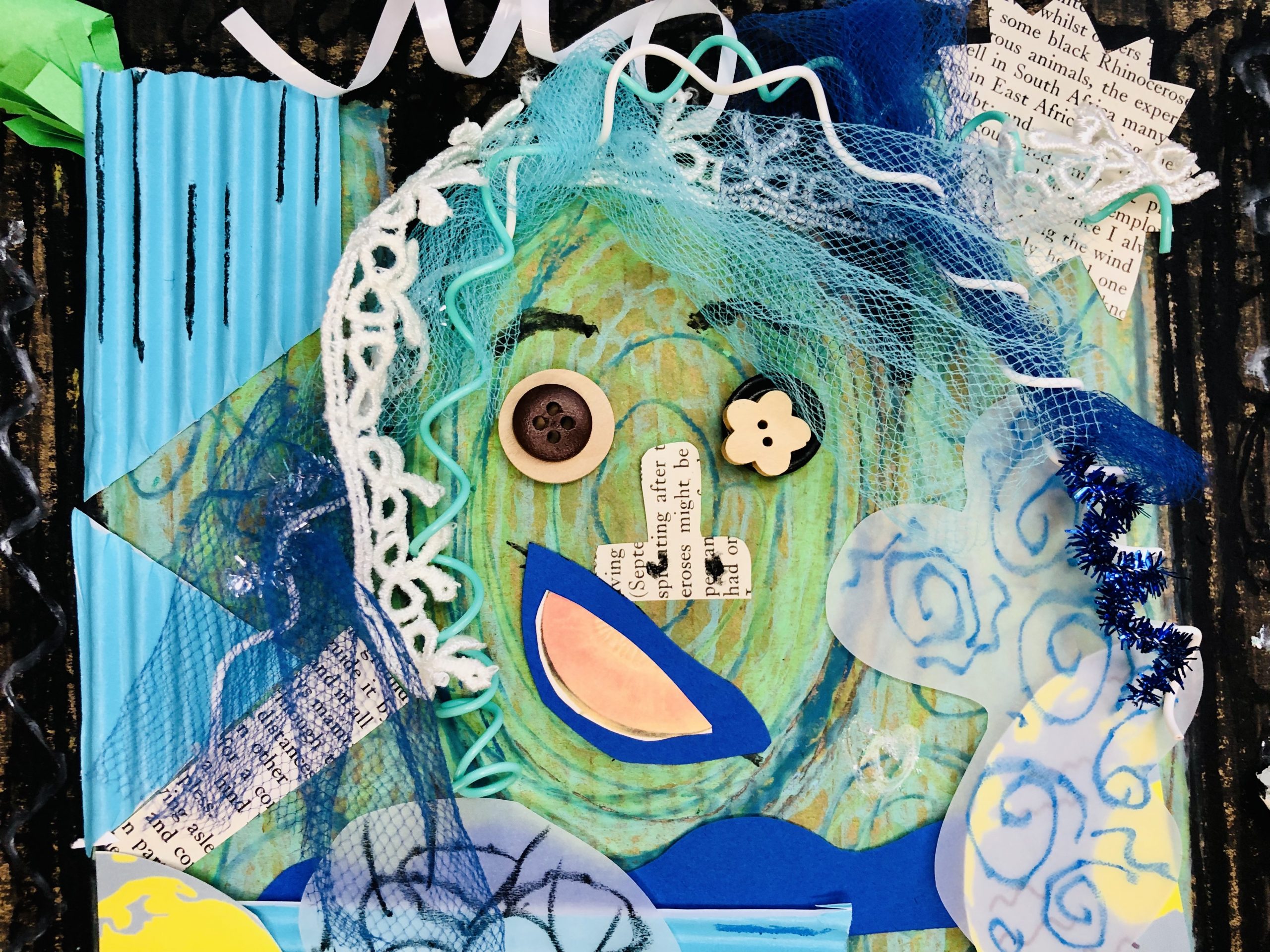 A mixed media artwork depicting an abstract human form with its hands raised above their head. The portrait includes hair of curly wire, ribbon, tulle, and chenille sticks in shades of white, blue, and teal. The face has eyes made of buttons, a nose made from newspaper, and a mouth made out of a photograph of a cantaloupe. The rest of the body is made with shades of blue, green, and black on a black background.