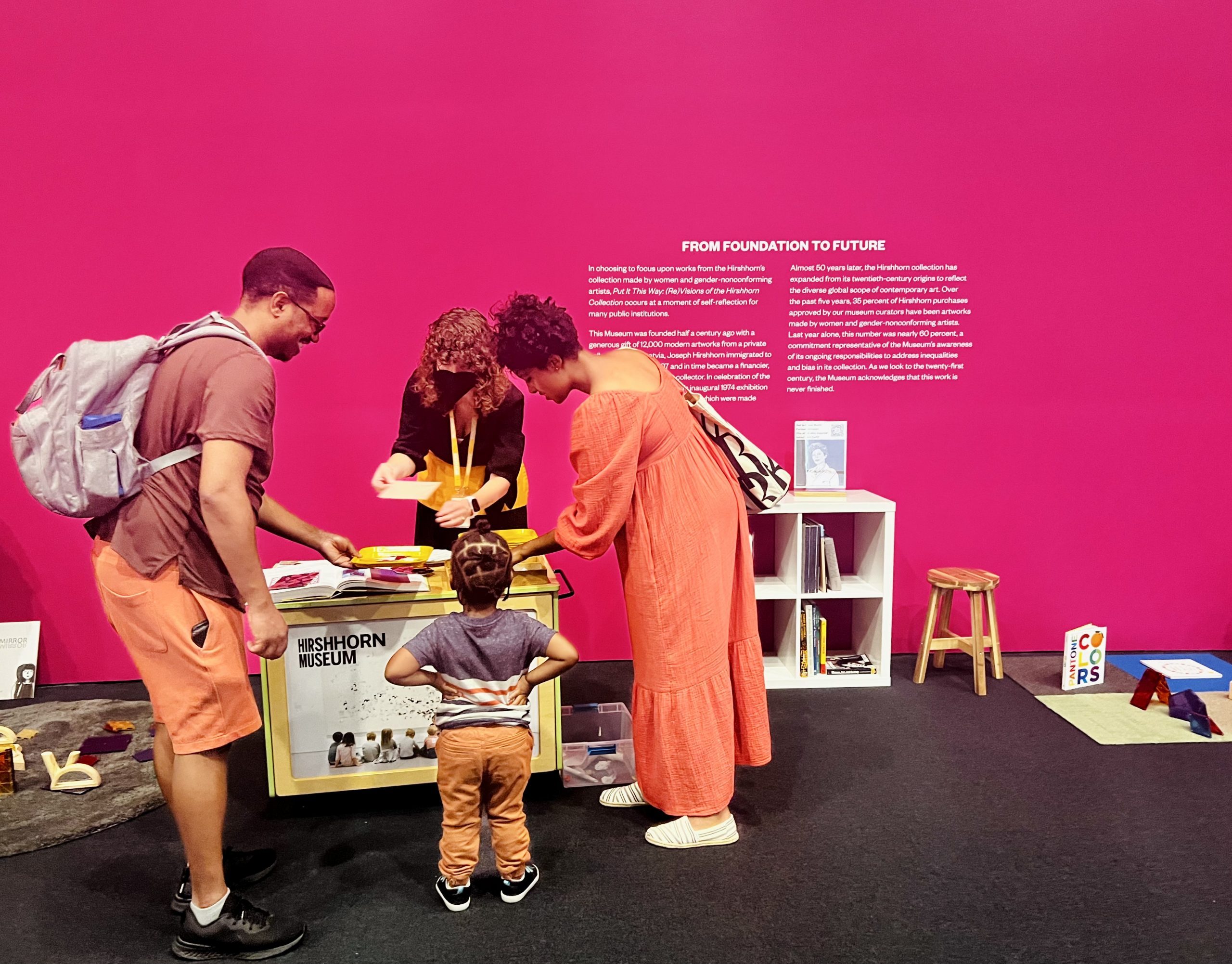 Two adults and a child interact with an educator at the art cart, placed in the activity section of the Put it This Way exhibit.