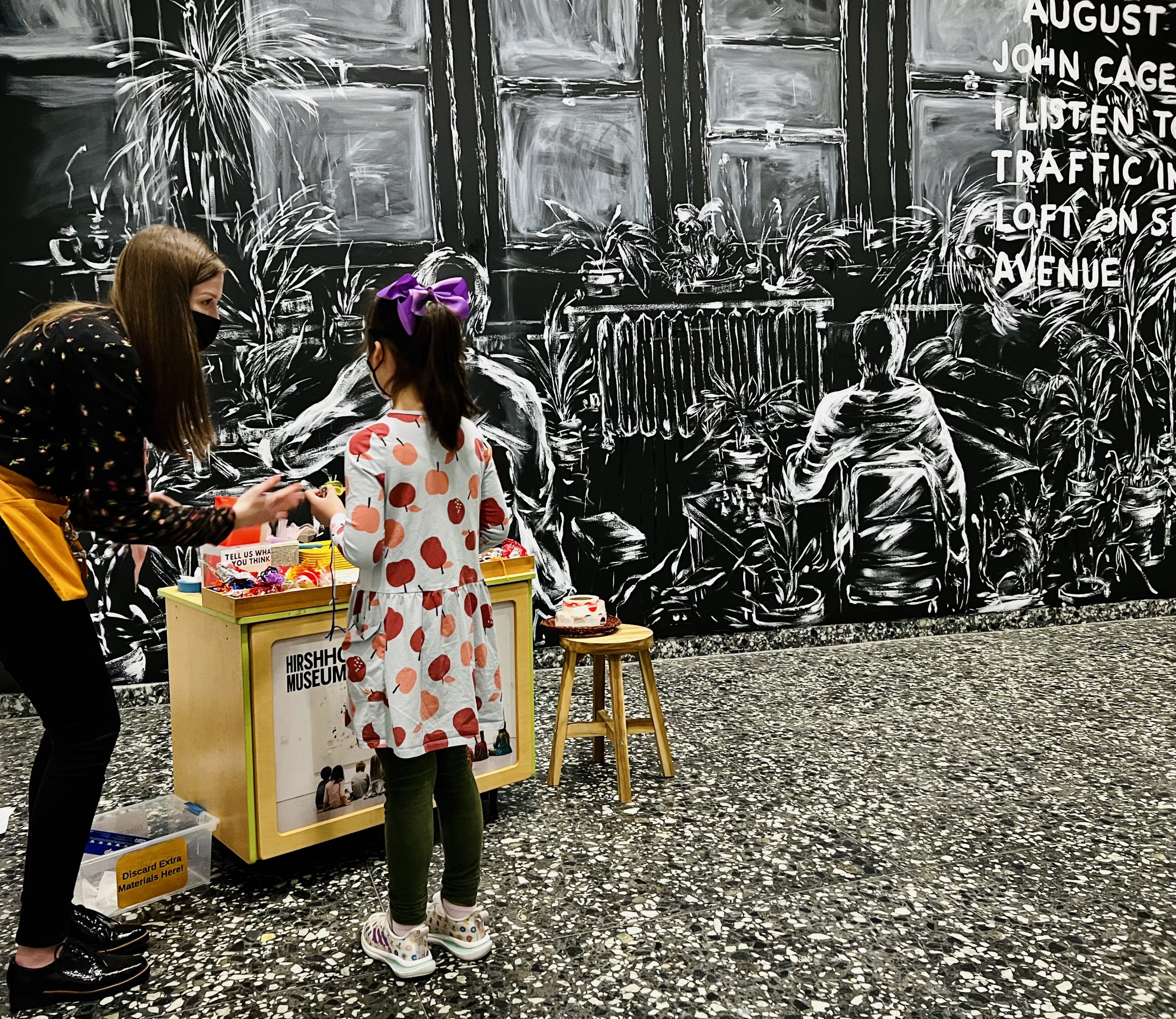 An educator leans down to talk to a kid outside Laurie Andersons : The Weather Exhibit.