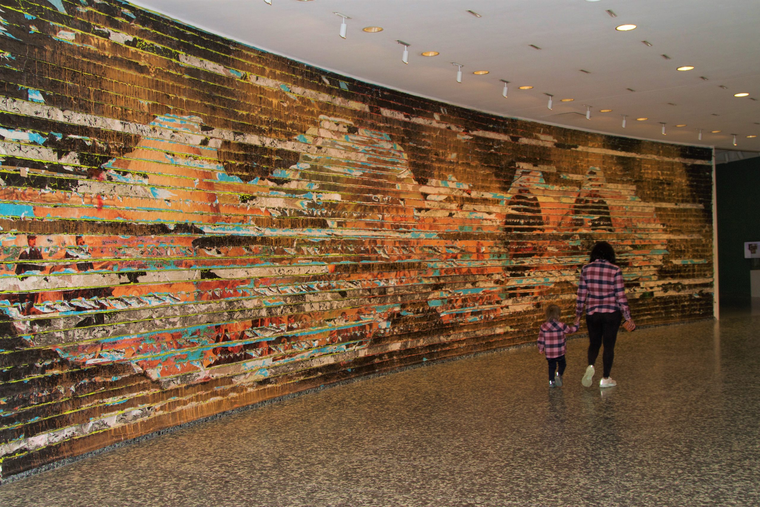 An adult and child walk hand-in-hand through the Mark Bradford: Pickett's Charge inner ring gallery.