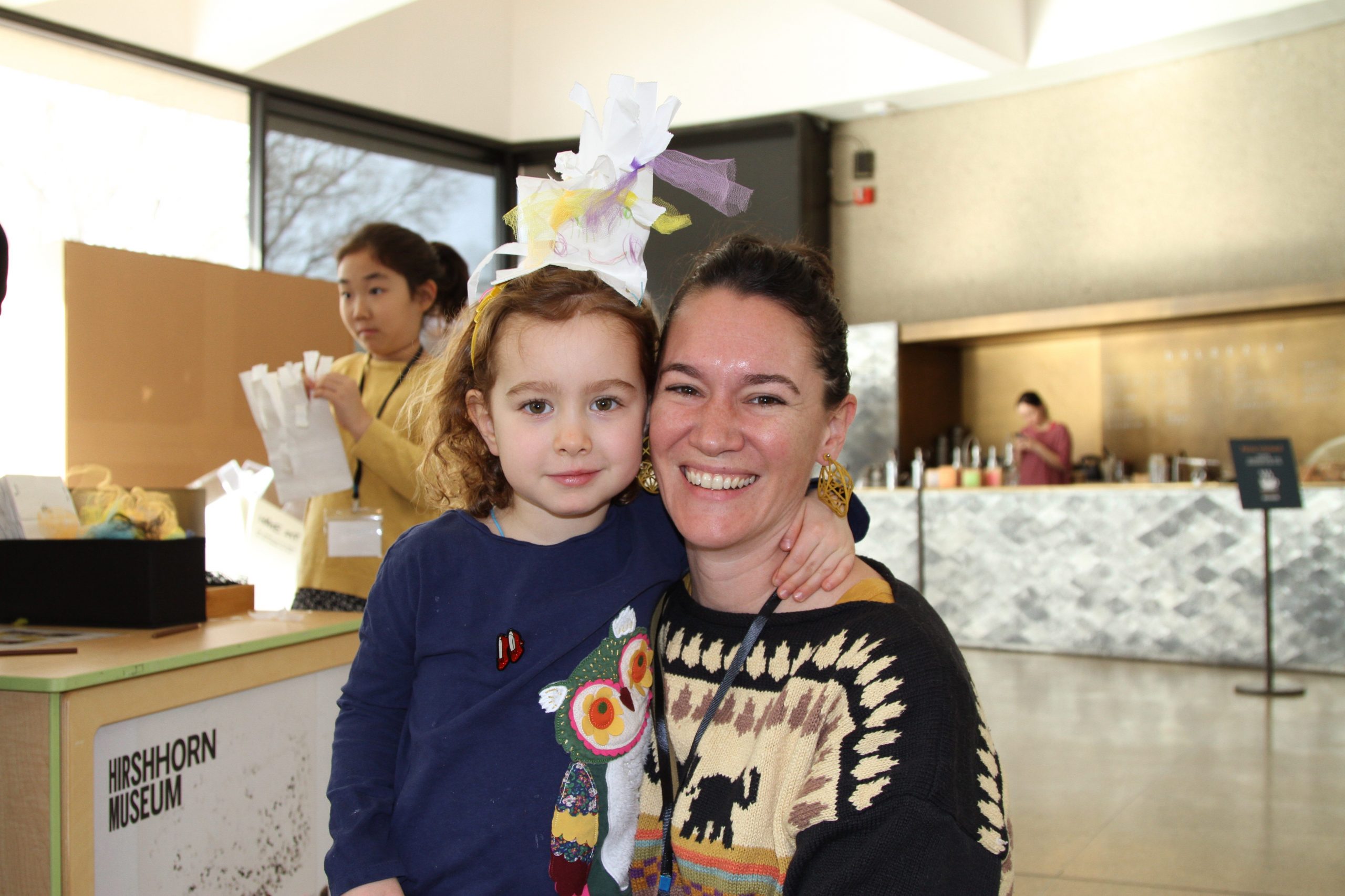 A child and her adult caretaker smile directly at the camera in the Hirshhorn's lobby.