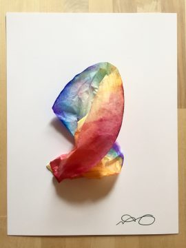 A multi-colored tie dyed coffee filter is stapled to a white piece of paper, an artists signature on the bottom right.