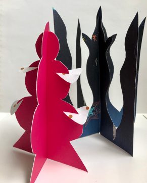 Two colored used cardboard pieces have been cut out into vaguely tree-like shapes to form small sculptures.