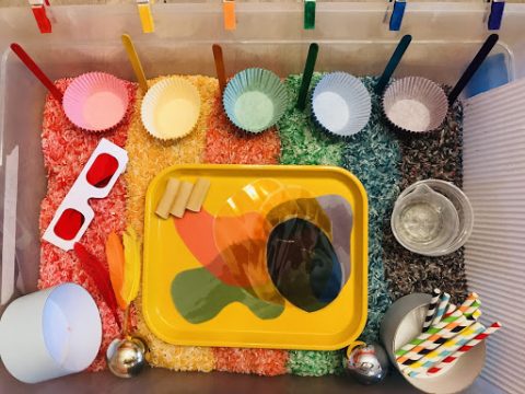 Birds eye view of the inside of a plastic bin containing six verticle rows of colored rice that make up a rainbow.