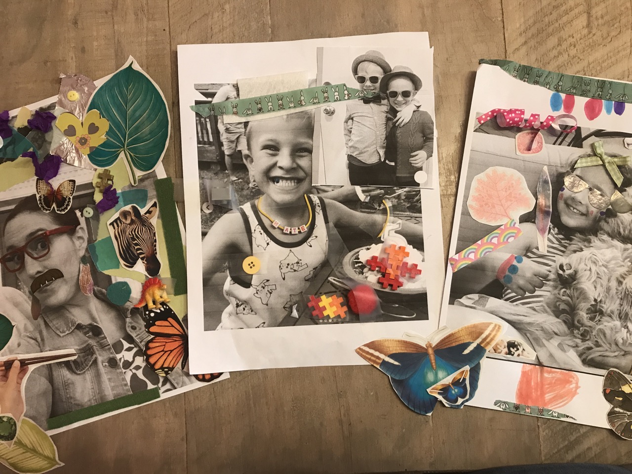 Three collaged self portraits with black and white photographs and colorful additions on pieces of paper laying beside each other on a wooden surface.