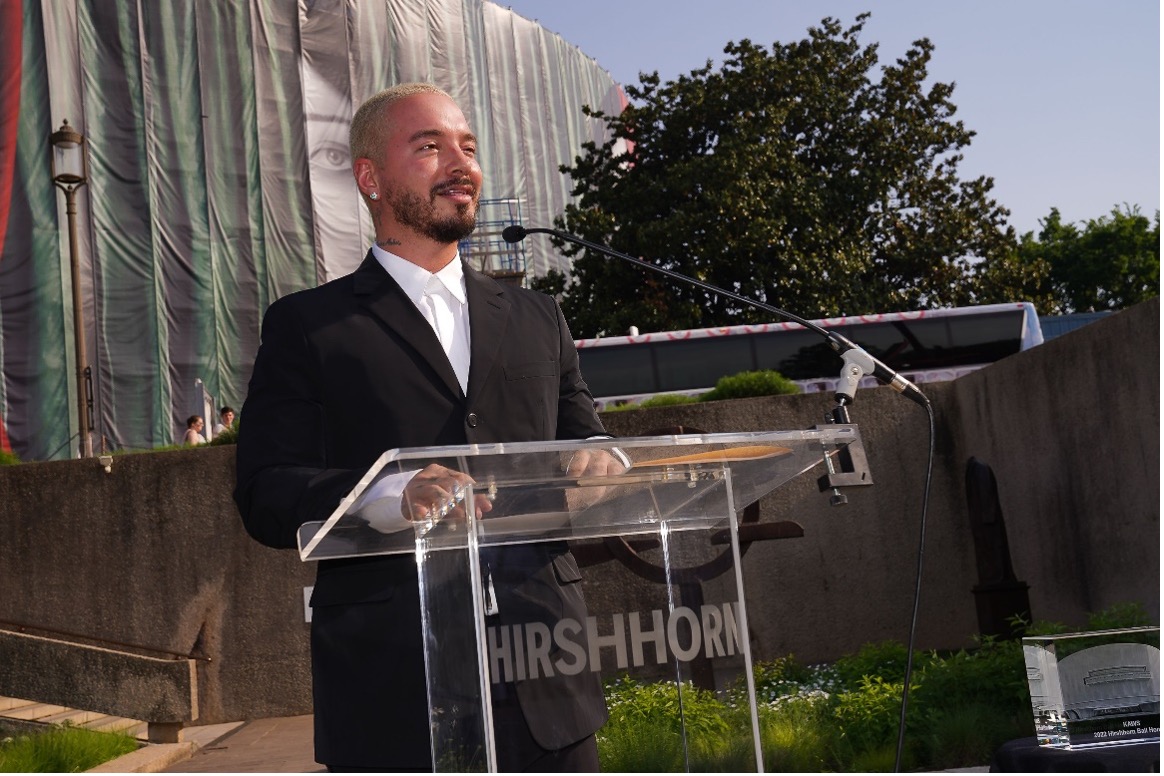 Singer J Balvin stands in front of a Hirshhorn branded podium in the Hirshhorn Sculpture Garden