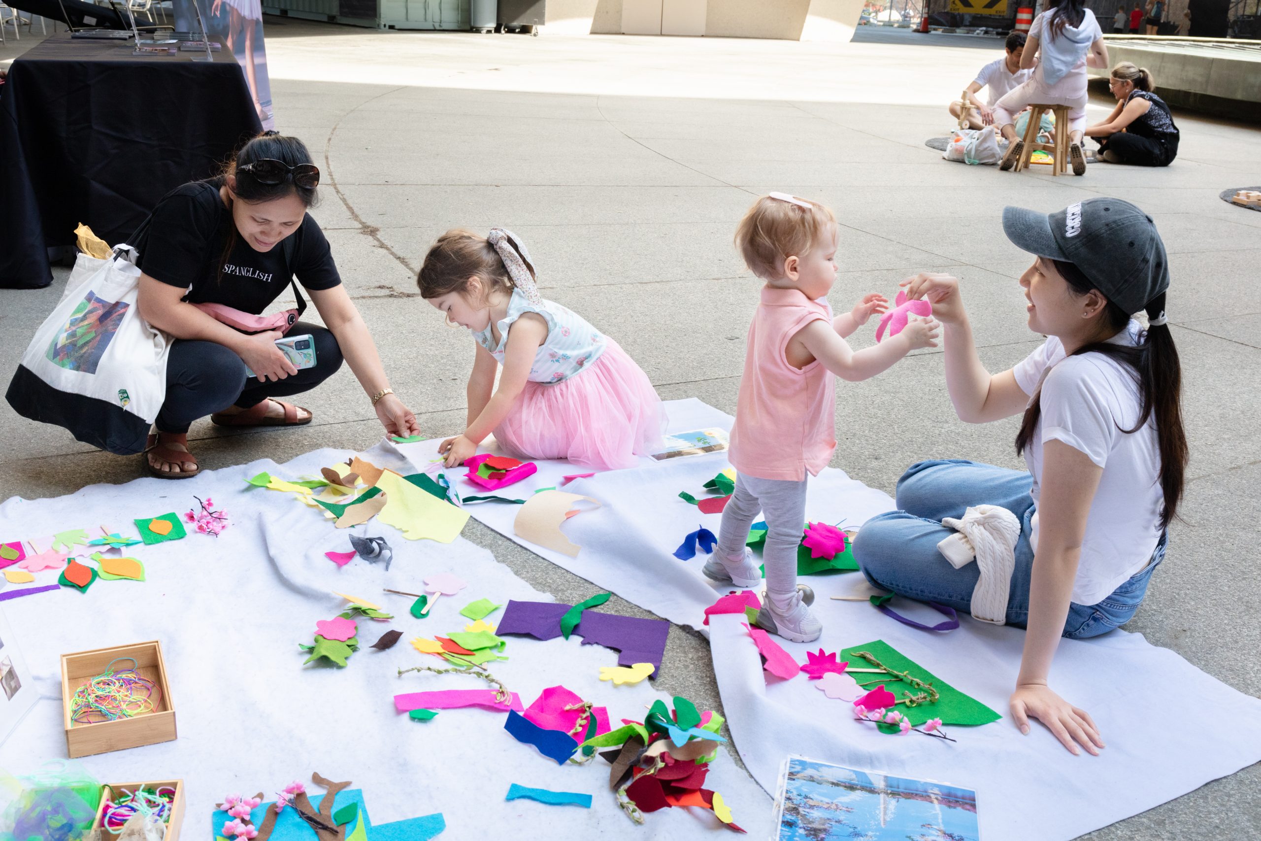 Two children in pink interact with their respective caretakers on the Hirshhorn's plaza.