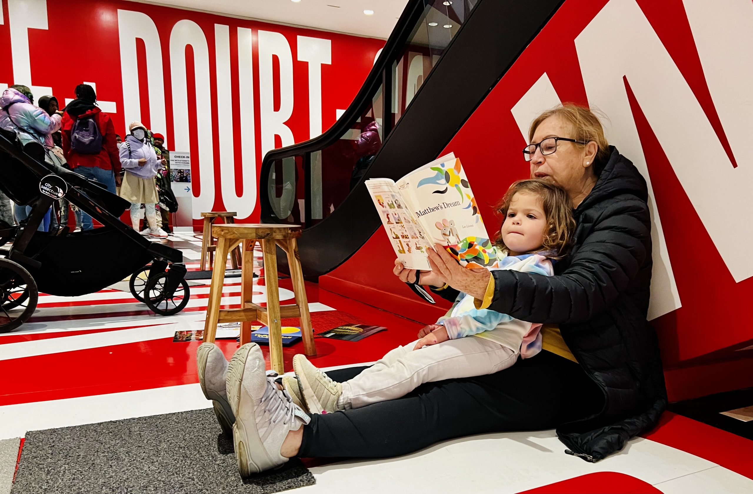 caregiver and child reading a book on the side of the barbara kruger escalator.