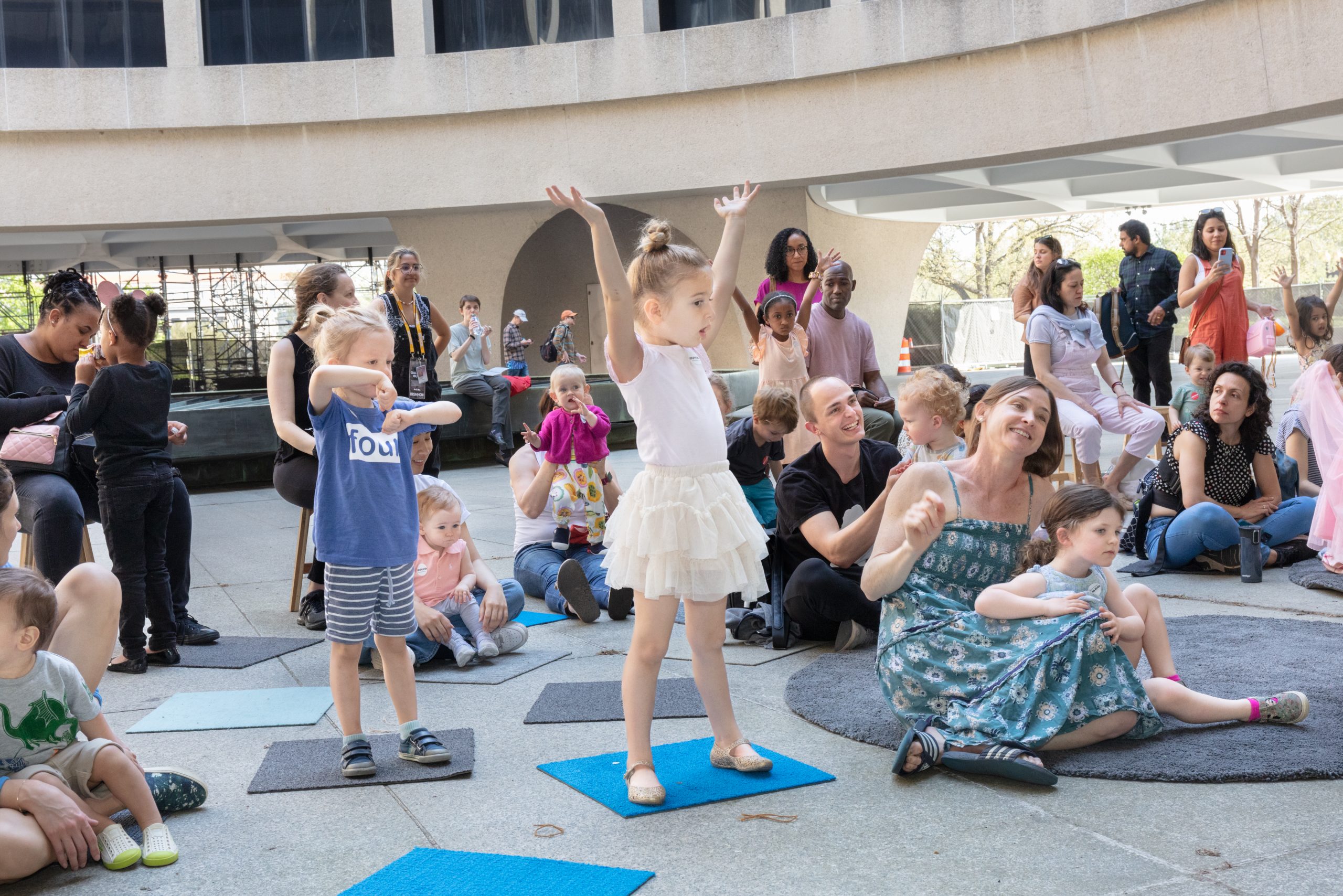 Children stand on small mats with their arms outstretched as part of an education event on the Hirshhorn's Plaza.