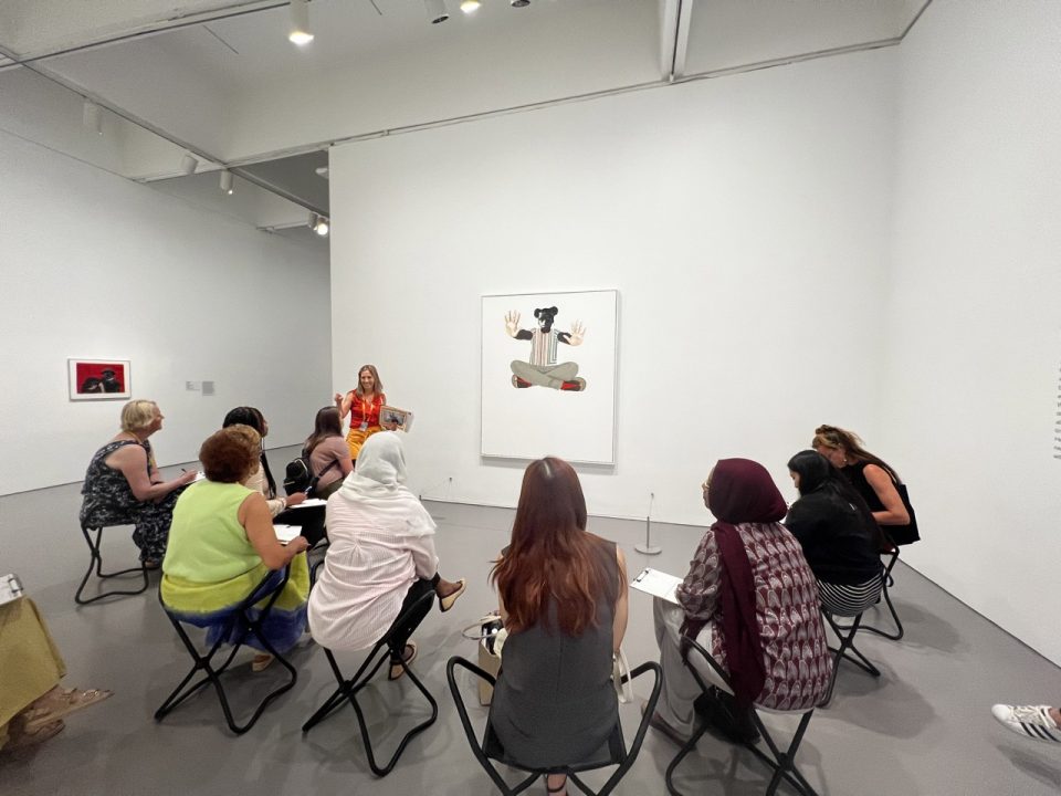 Instructor with visitors in gallery sitting in front of artwork