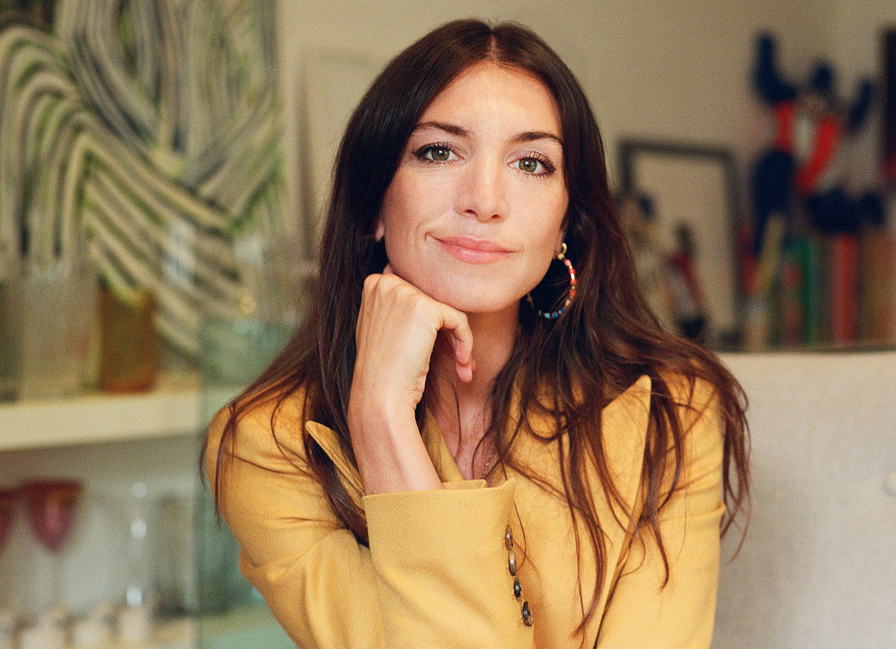 a woman wearing a yellow blazer smiles with her chin resting on her right hand