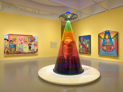 a colorful sculpture of an alien abduction, surrounded by colorful paintings.