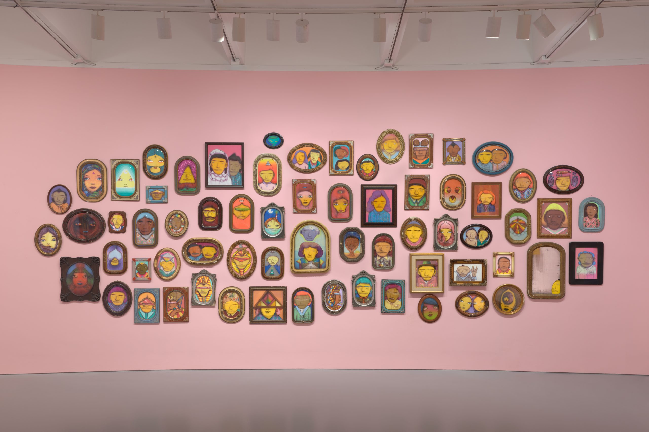 a large group of painted portraits displayed on a pink wall.