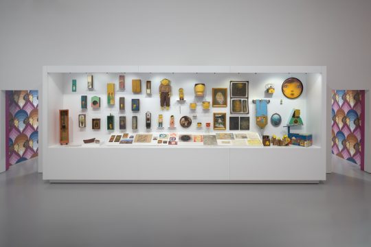 a large white case featuring painted objects from the archive of Brazilian artists OSGEMEOS