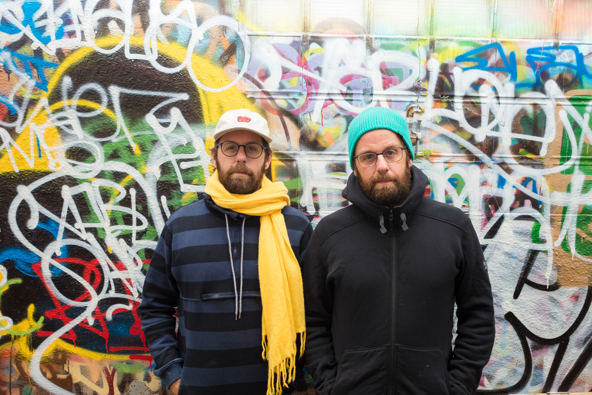 two Brazilian artists posing in front of a wall covered in graffiti