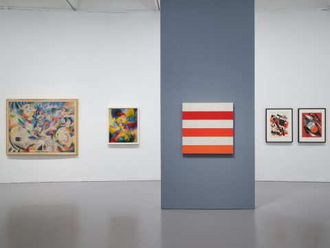 five abstract paintings are displayed in a gallery, the first two on the left feature colors of green, blue, purple and yellow shapes, the next three paintings on the right feature red, orange, and white shapes.