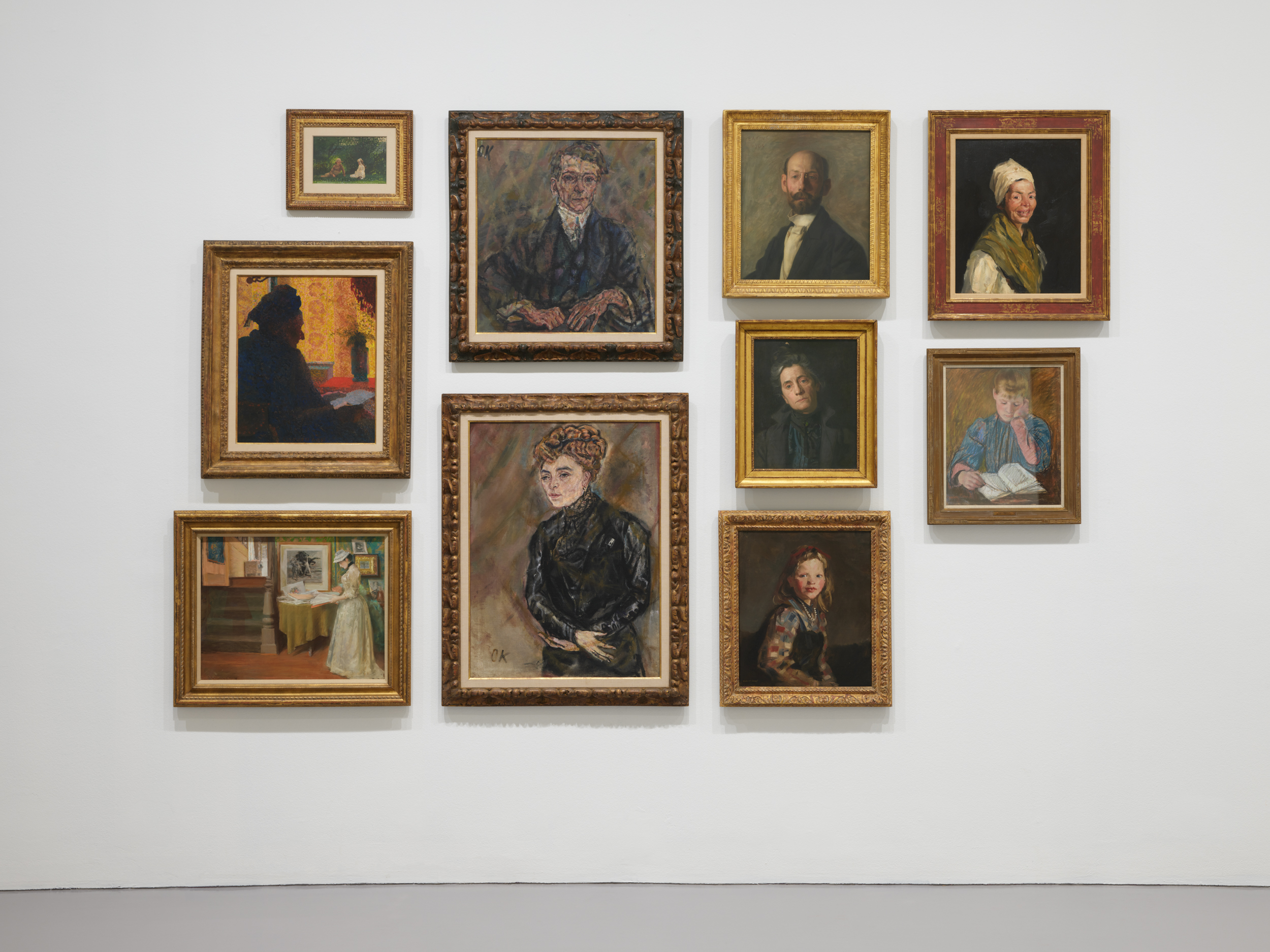 a wall covered in 12 small and medium portraits of white men, women and children.